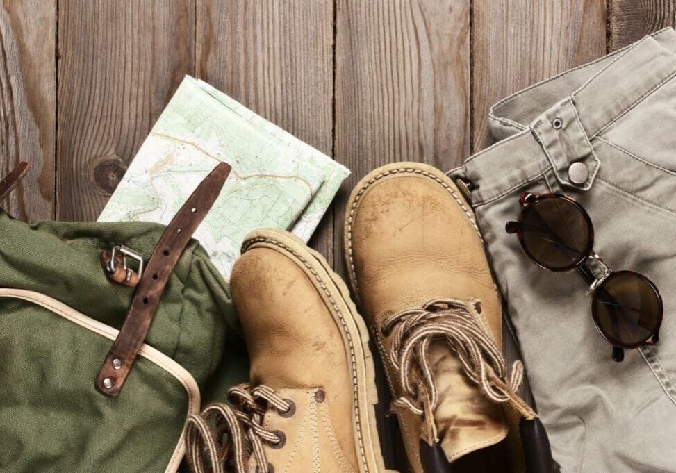 A pair of boots, sunglasses and some clothing on the ground.